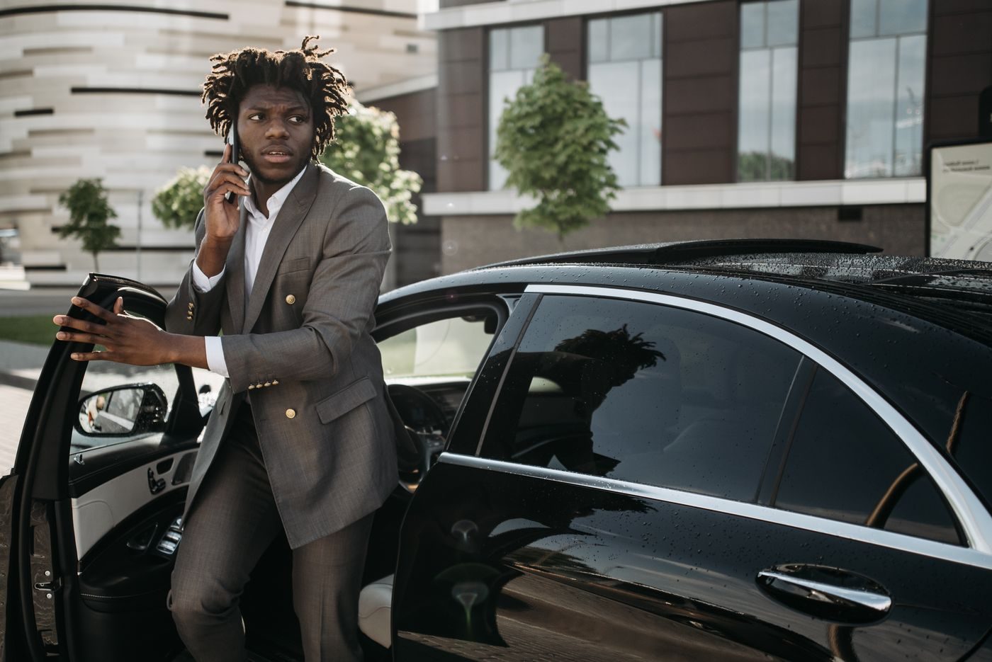 Businessman on the phone stepping out of a black car outside an office building